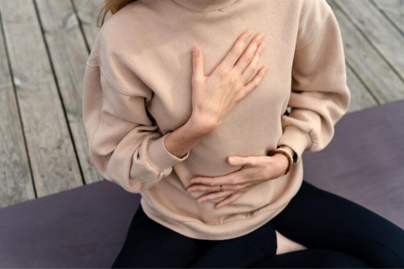 Atemübung zur Entspannung | Frau legt eine Hand aufs Herz und eine auf den Bauch