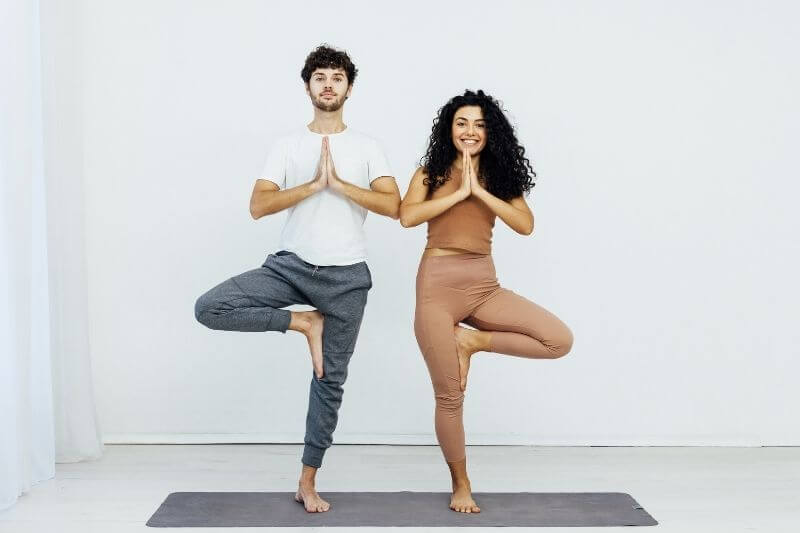 Paar übt den Baum zu zweit auf der Yoga-Matte