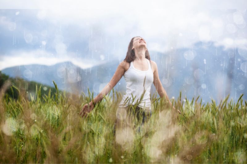 Frau tanzt im Regen auf Wiese